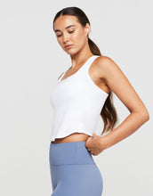 Woman wearing a white sleeveless top and light blue leggings on a plain background