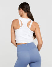 Woman wearing a white sports bra and blue leggings on a light gray background