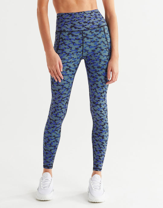 A woman wearing blue printed leggings with white runners on a white background.