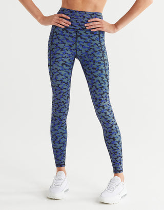 A woman wearing blue printed leggings with white sneakers on a white background.