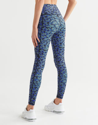 A woman wearing blue abstract printed leggings with white runners on a white background.
