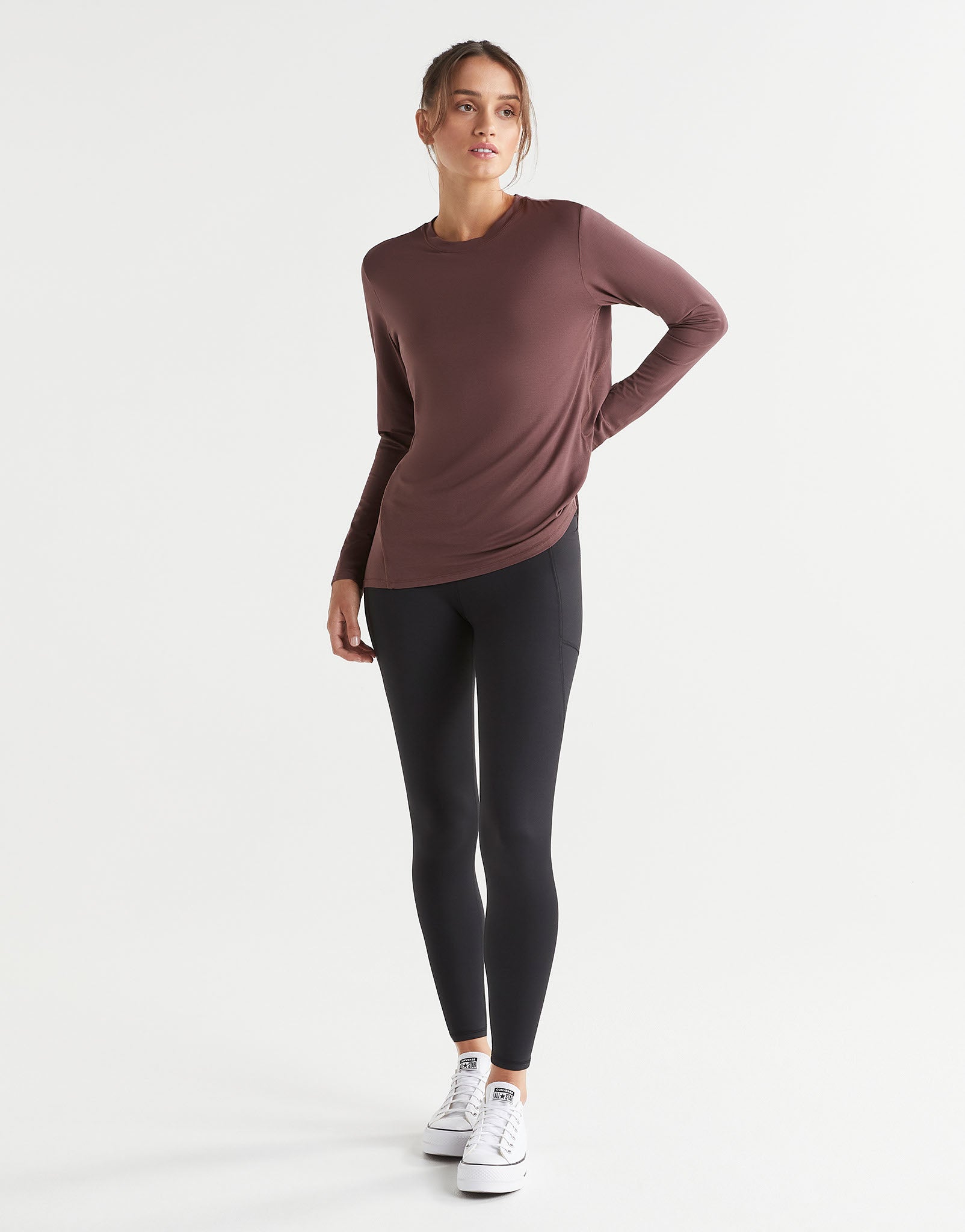 Woman wearing a brown long-sleeve top and black leggings on a white background