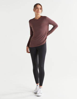 Woman wearing a brown long-sleeve top and black leggings on a white background