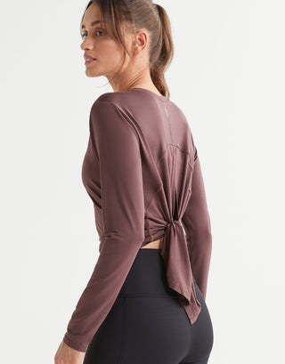 Woman wearing a mauve long-sleeve top with a knot detail on a white background