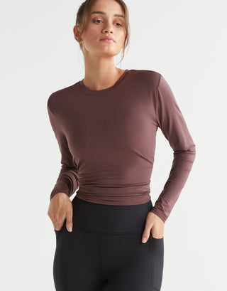 Woman wearing a brown long-sleeve top and black leggings on a light gray background