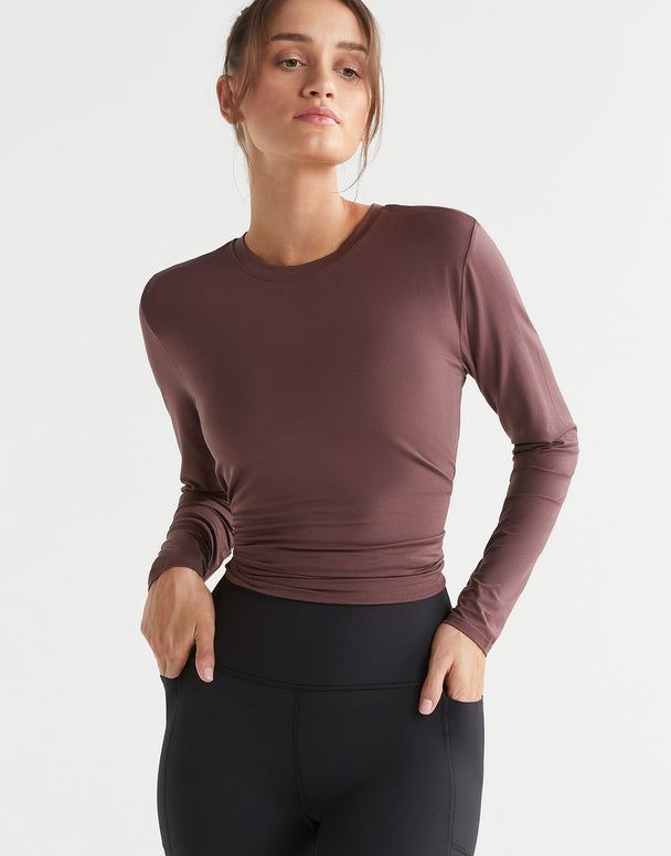 Woman wearing a brown long-sleeve top and black leggings on a light gray background