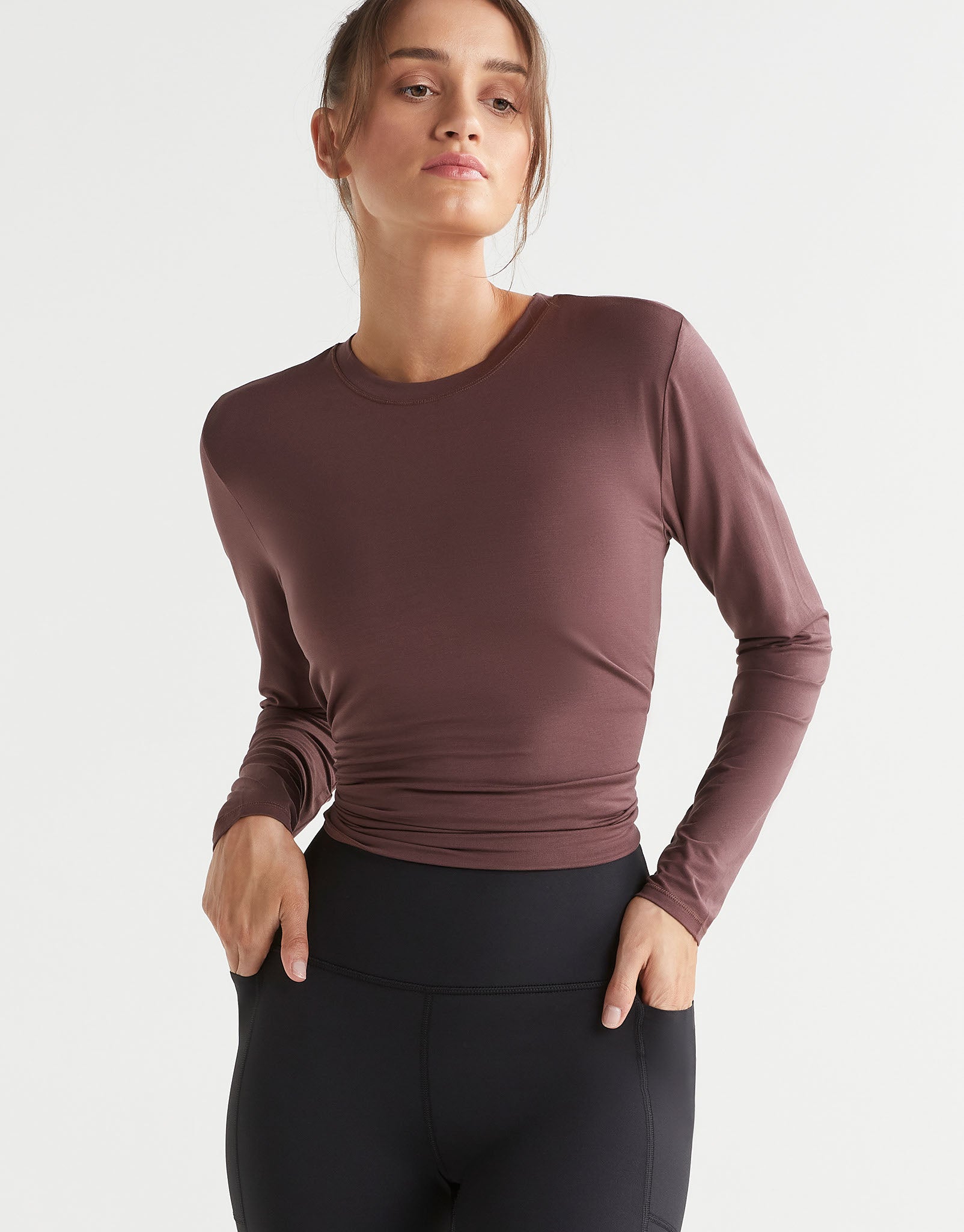 Woman wearing a brown long-sleeve top and black leggings on a light gray background