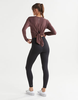 Woman wearing a brown long-sleeve top and black leggings on a white background