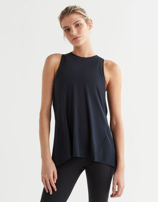 A woman modeling a sleeveless athletic tank top in dark navy blue, paired with black leggings, against a plain light gray studio background.