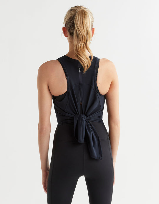 Person wearing a black sleeveless top with a knot detail on a light gray background