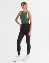 Woman wearing a green tank top and black leggings on a white background