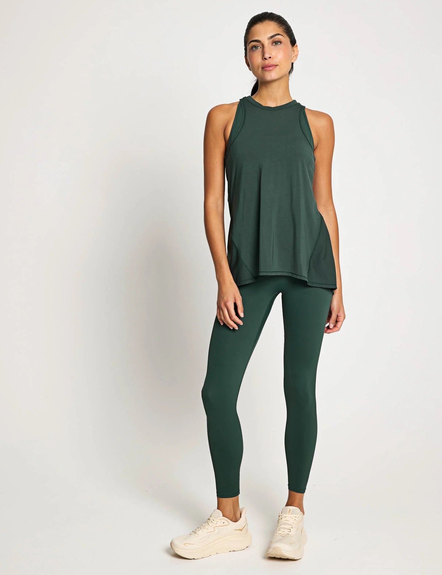 Woman wearing a green sleeveless top and leggings on a white background