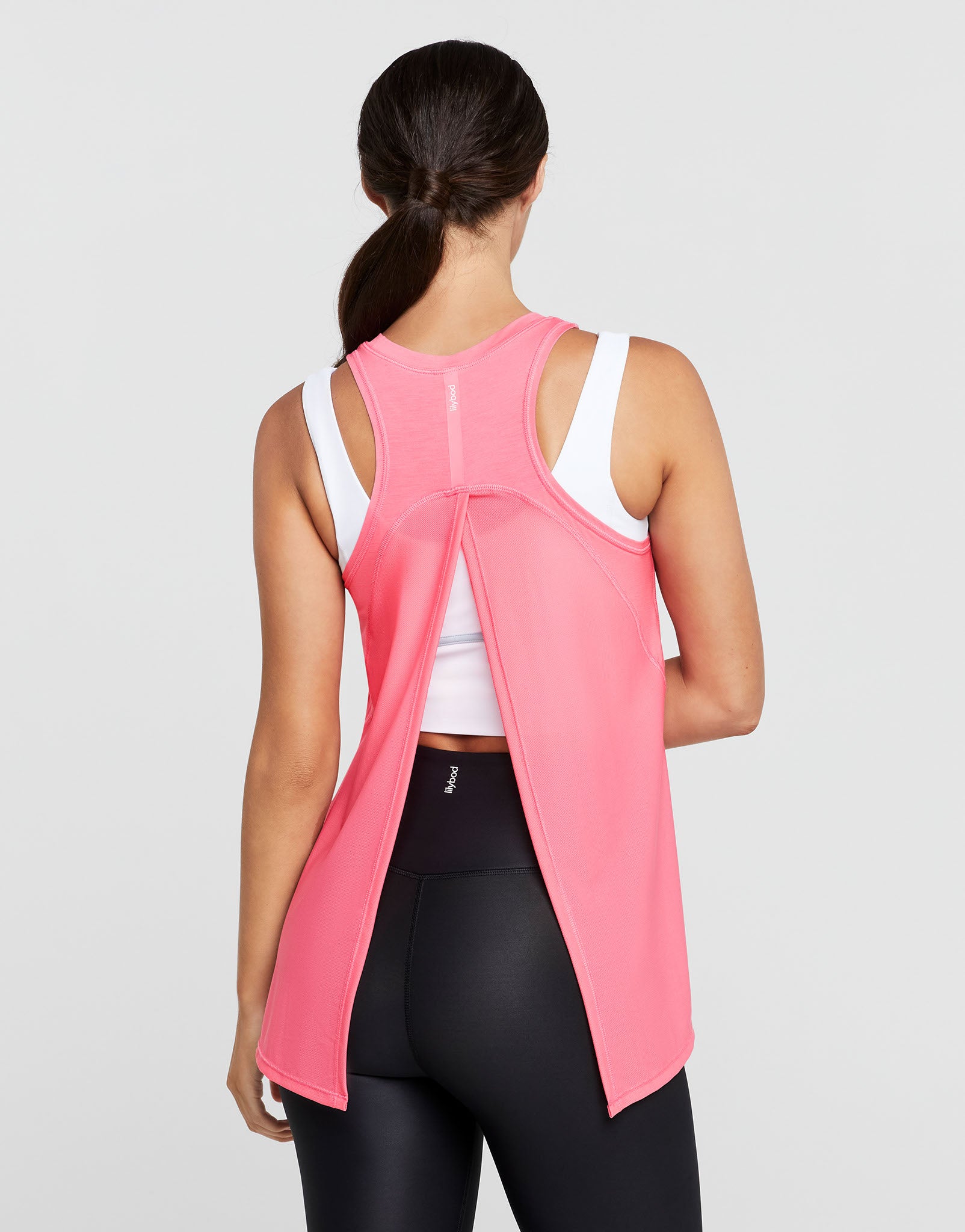 Woman wearing a pink sleeveless top with a white shirt underneath on a gray background