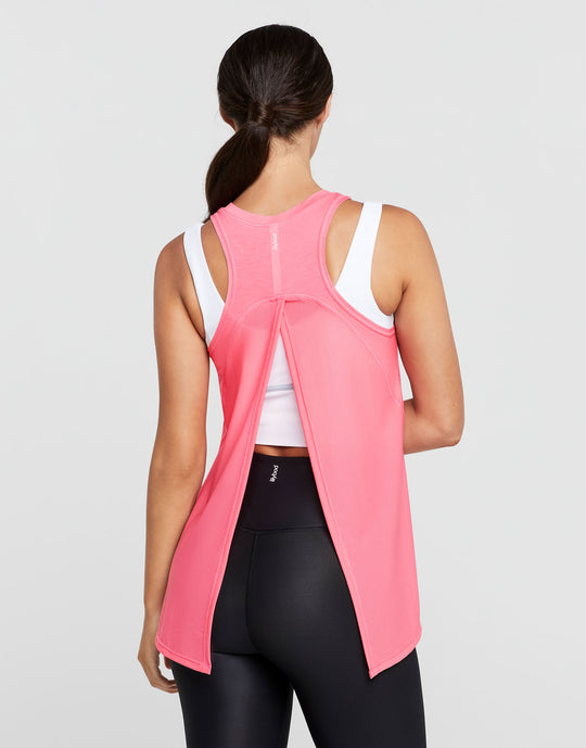Woman wearing a pink sleeveless top with a white shirt underneath on a gray background