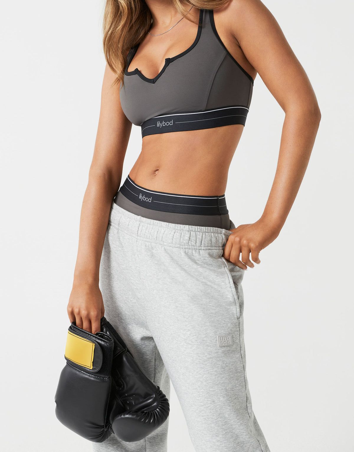 A woman wearing grey sweatpants and a sports bra with boxing gloves.