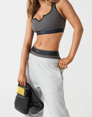 A woman wearing grey sweatpants and a sports bra with boxing gloves.