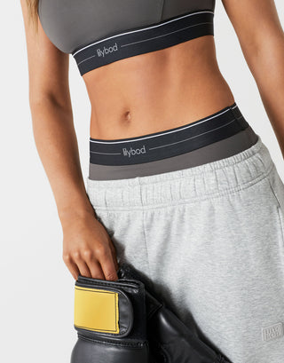 Person wearing a gray sports bra and pants with Flybod branding, holding a black and yellow weightlifting belt.