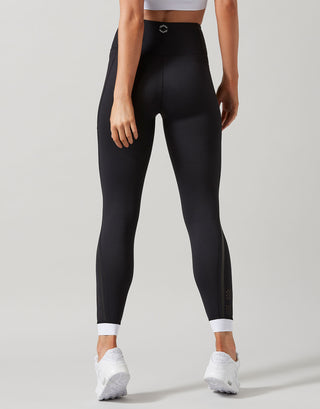 Person wearing black leggings with white accents on a plain background