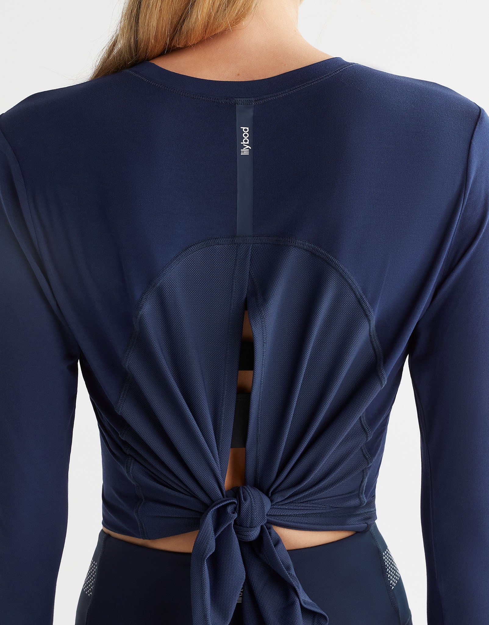 Close up of a woman wearing a navy blue long sleeved top which is tied up at the back with a logo on it