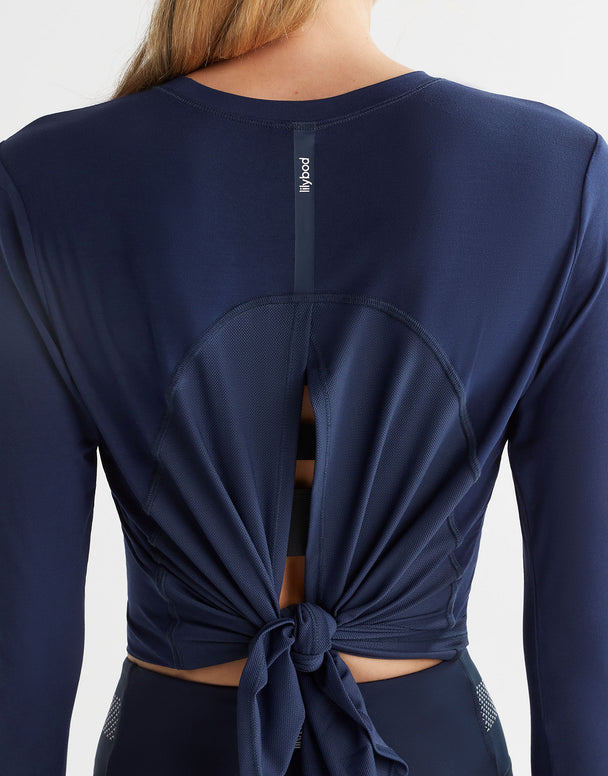 Close up of a woman wearing a navy blue long sleeved top which is tied up at the back with a logo on it