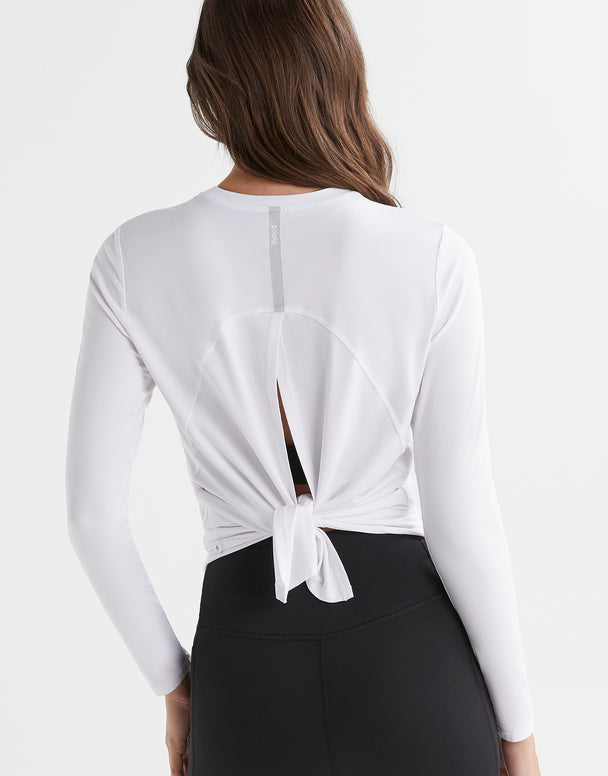 A woman wearing a bright white long sleeved activewear top with a relaxed fit. The top has a crew neckline and a split back.