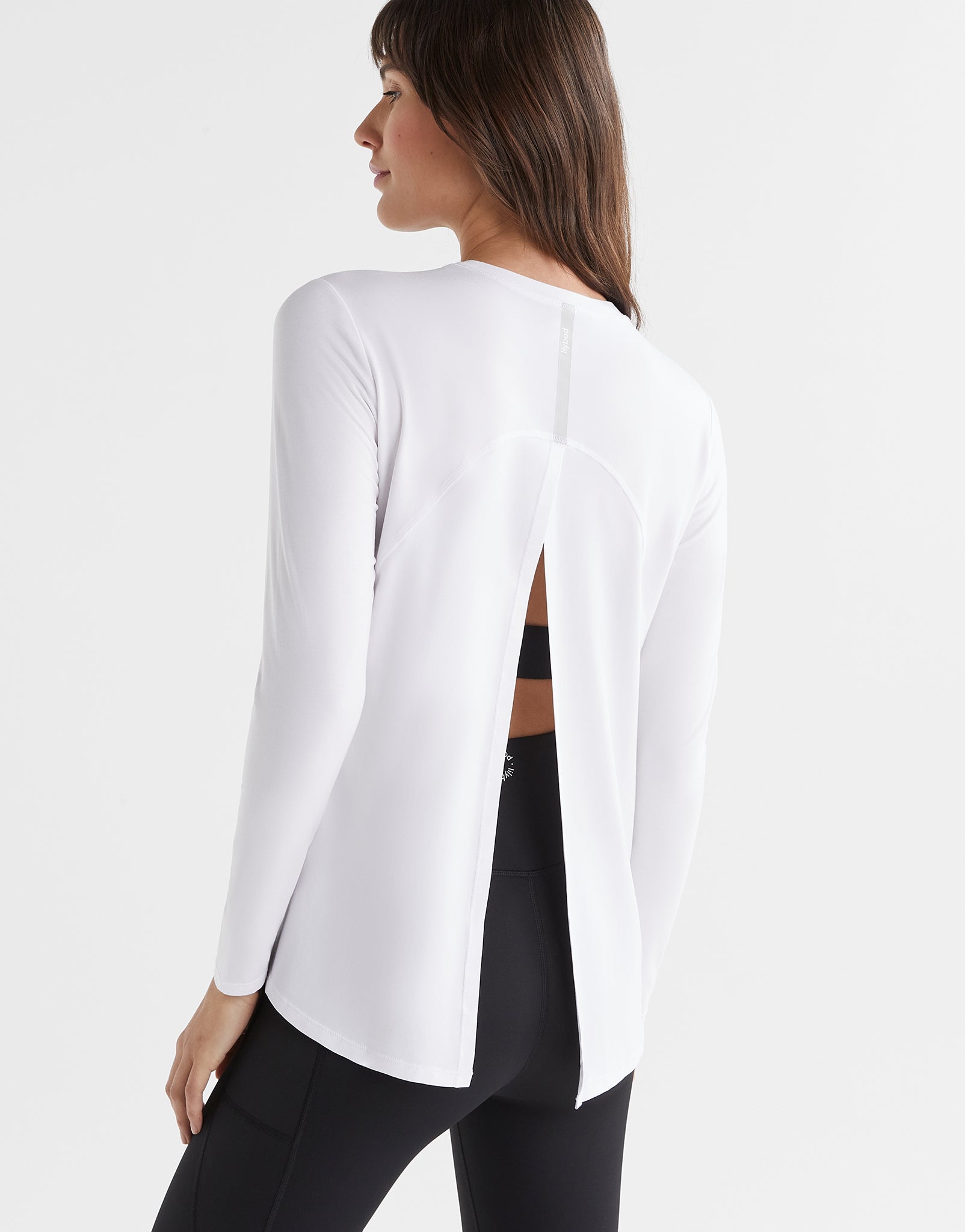 Woman wearing a white long-sleeve top and black leggings on a light gray background