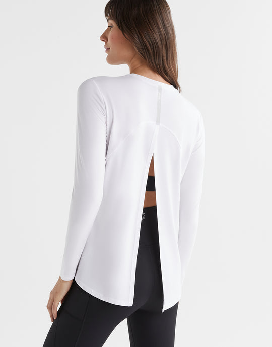 Woman wearing a white long-sleeve top and black leggings on a light gray background