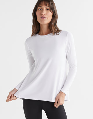 A woman wearing a bright white long sleeved activewear top with a relaxed fit. The top has a crew neckline and a split back that can be tied or left open.