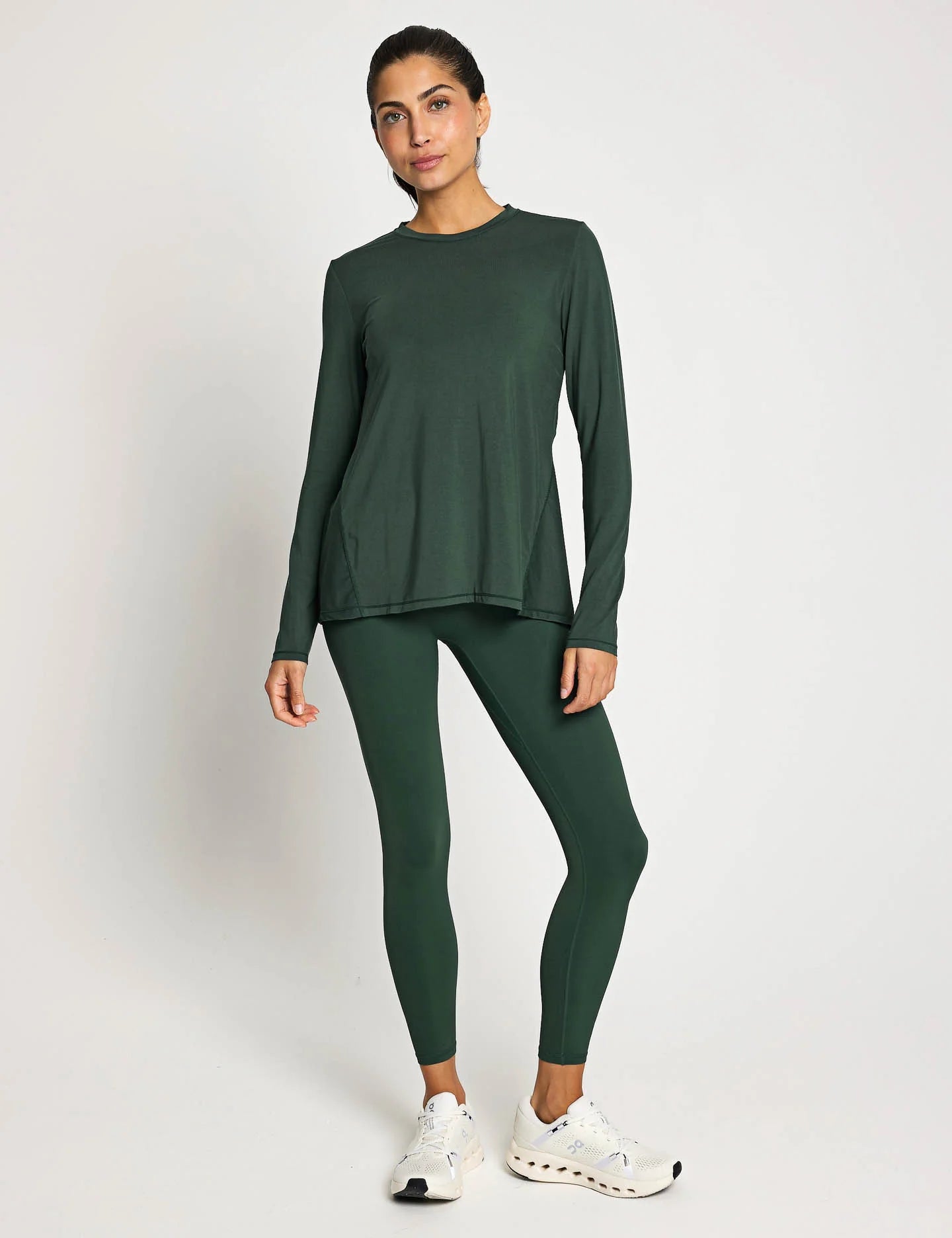 Woman wearing a green long-sleeve top and leggings on a white background
