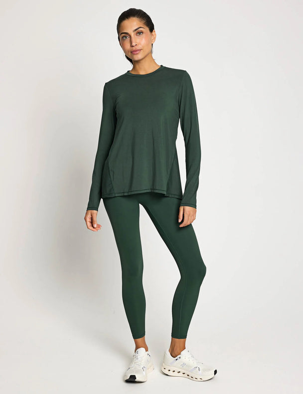 Woman wearing a green long-sleeve top and leggings on a white background