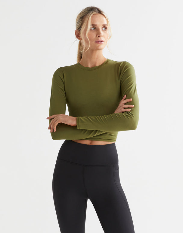 A female model wearing a long sleeved, tie-up top in army green, paired with black pants.