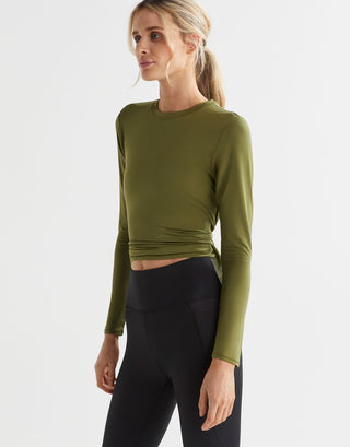 A woman wearing an army green long sleeve tie-up top with black leggings.