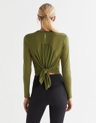 A female model wearing a long sleeved, tie-up top in army green, paired with black leggings.