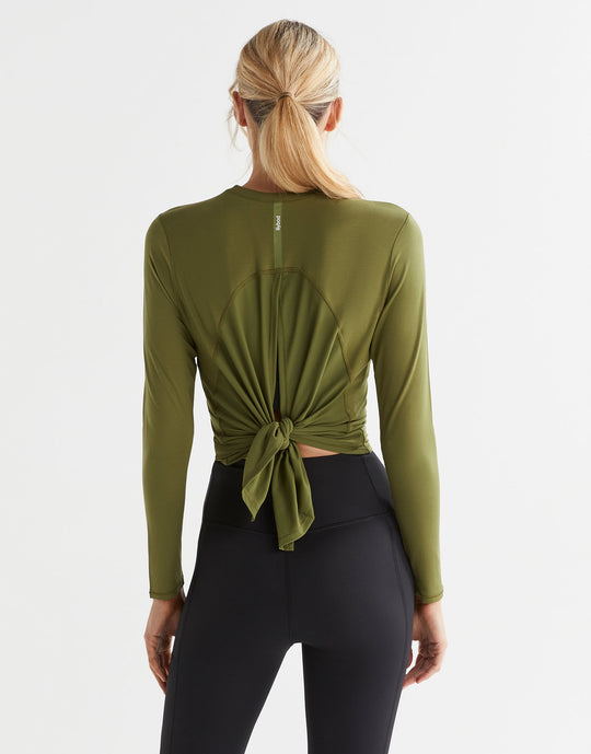 A female wearing an army green long sleeve tie-up top with black leggings.
