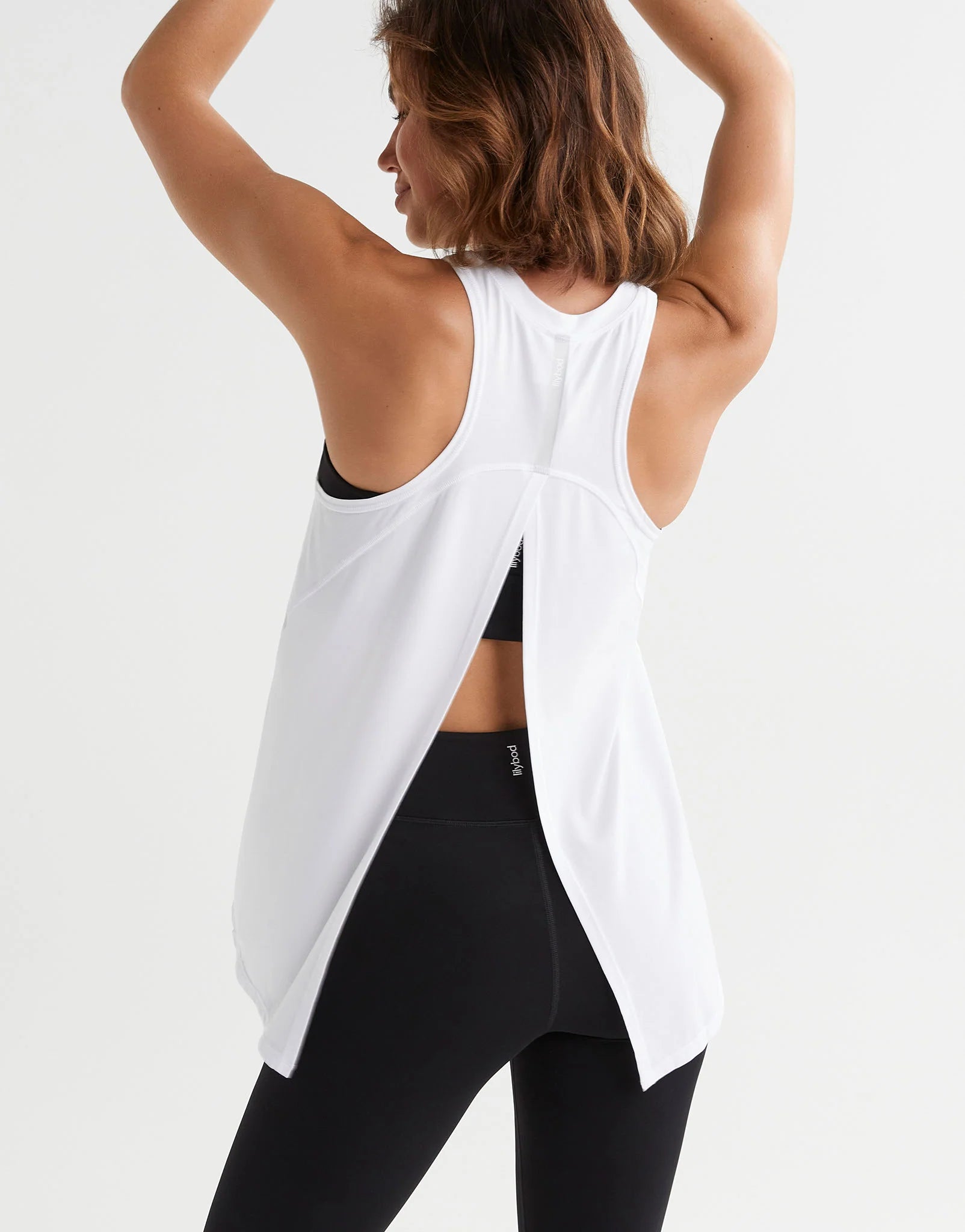 A woman wearing a white tank top and black leggings from the back.