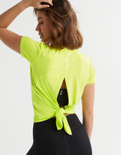 Woman wearing a bright green athletic top with a tie detail on a white background