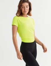 Woman wearing a bright green athletic shirt and black leggings on a light gray background