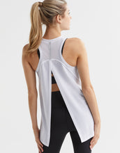 Woman wearing a white sleeveless top and black leggings on a light gray background