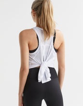 Woman wearing a white tank top with black trim and black leggings on a light gray background