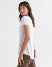 Woman wearing a white t-shirt with a side slit on a plain background