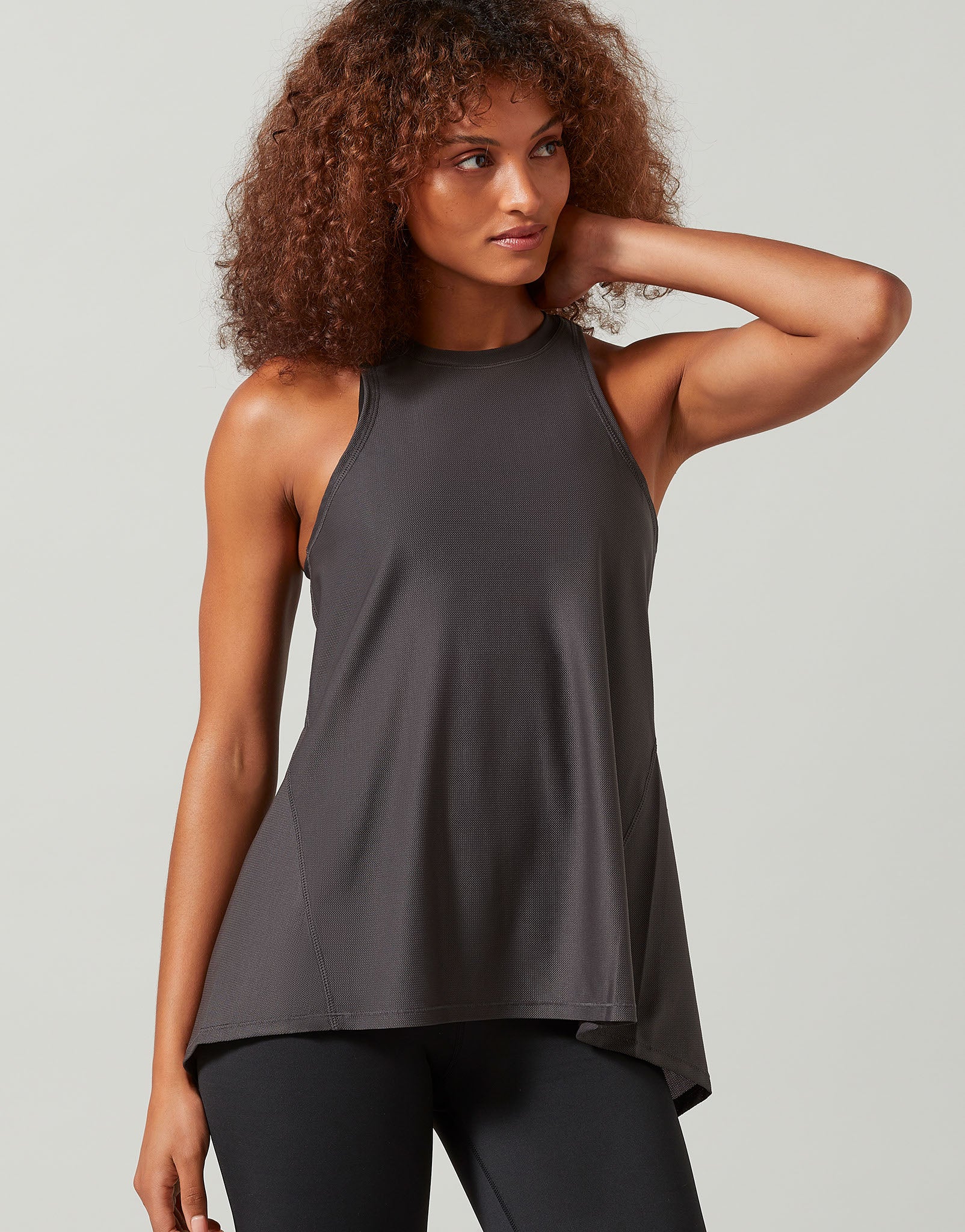 A woman wearing a grey tank top and black leggings on a white background