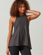 A woman wearing a grey tank top and black leggings on a white background