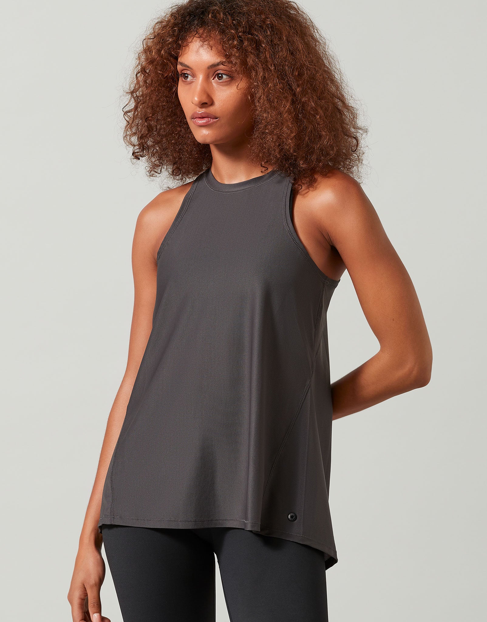 A woman wearing a grey tank top and black leggings on a white background