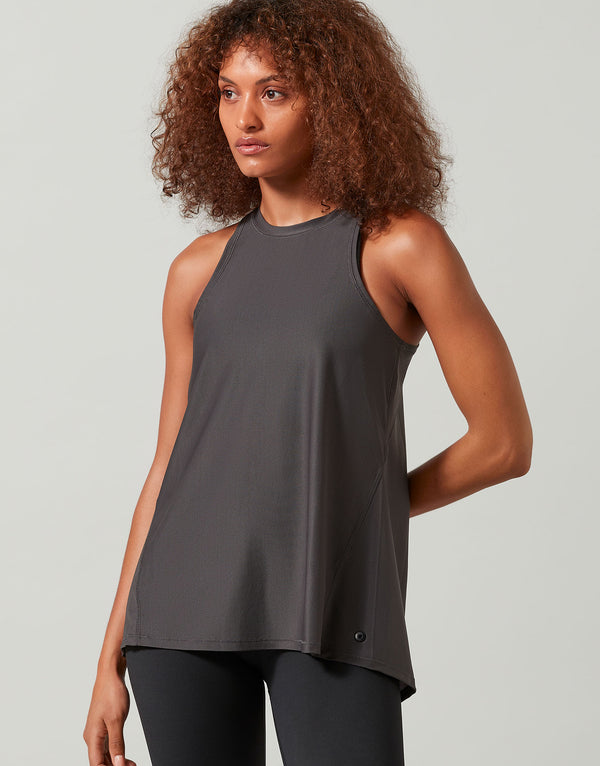A woman wearing a grey tank top and black leggings on a white background