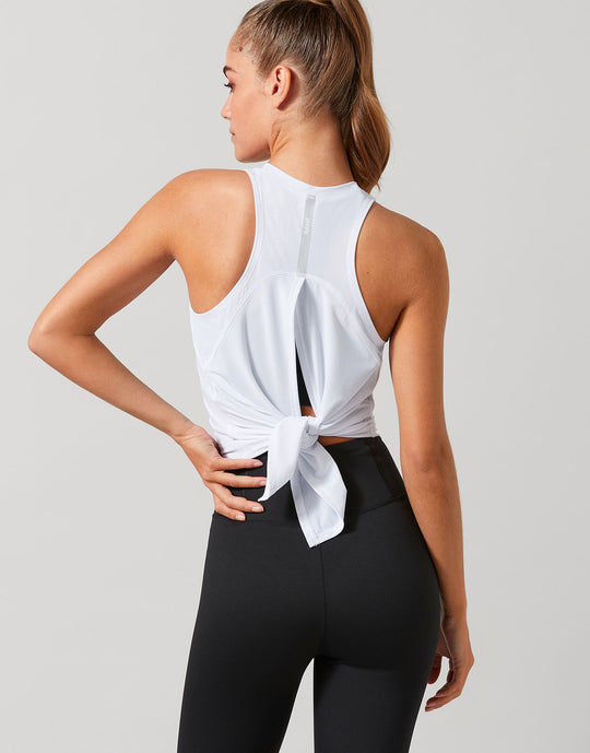 Woman wearing a white sleeveless top and black leggings on a light gray background