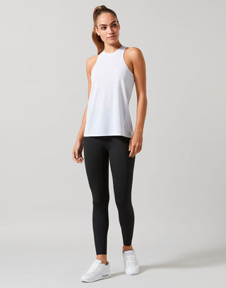 Woman wearing a white sleeveless top and black leggings on a light gray background