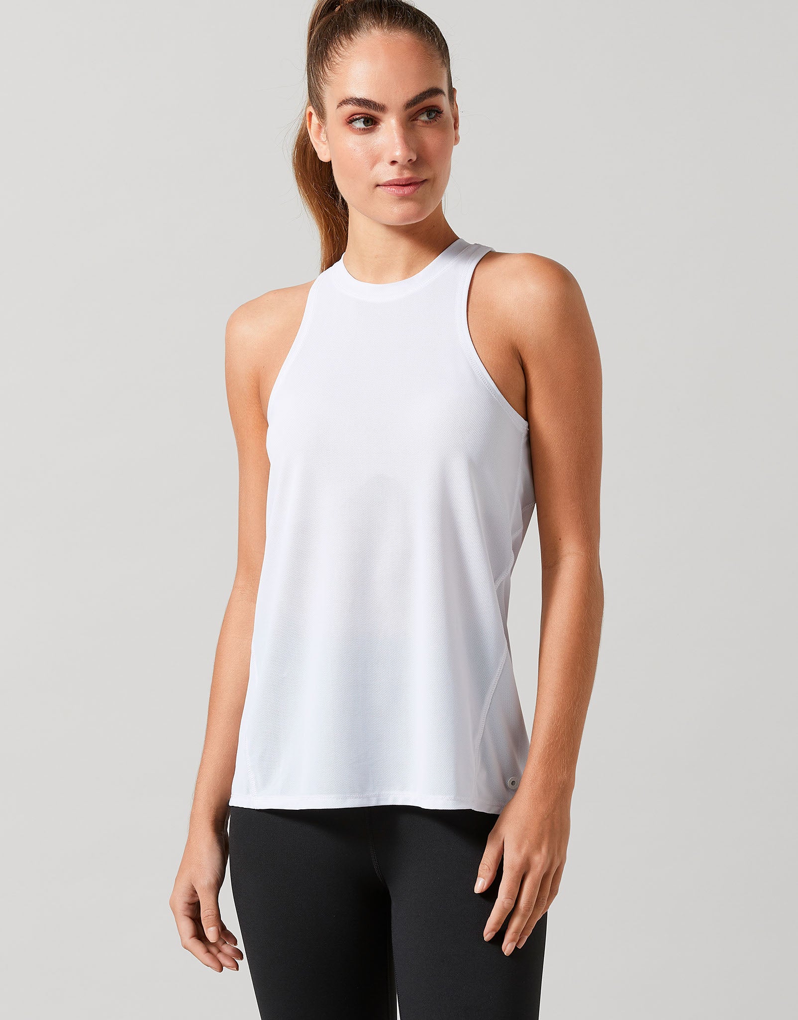 Woman wearing a white sleeveless top and black leggings on a light gray background