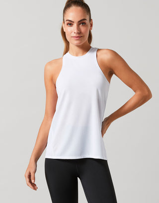 Woman wearing a white sleeveless top and black leggings on a light gray background
