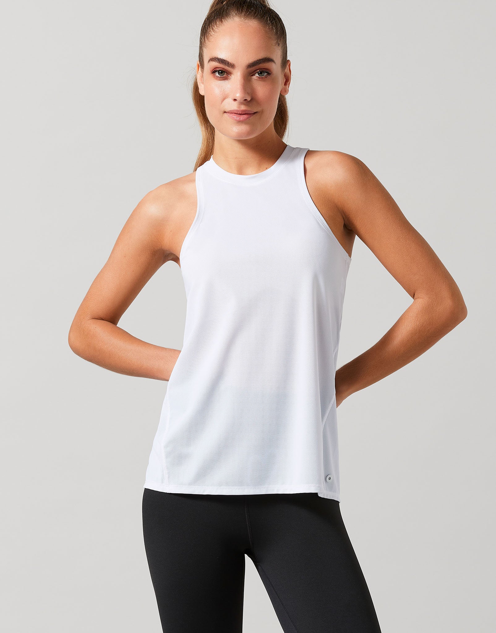 Woman wearing a white sleeveless top and black leggings on a light gray background
