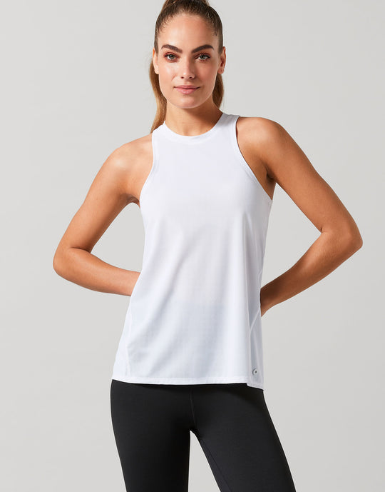 Woman wearing a white sleeveless top and black leggings on a light gray background